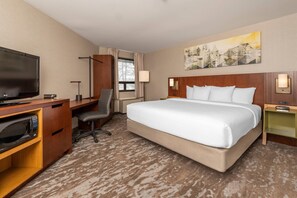 A hotel room with a large bed, a desk with a flat-screen TV, a microwave, and a chair.