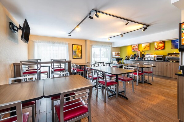 A modern dining area with multiple tables and chairs, a kitchen area with cooking equipment, and a wall-mounted television.