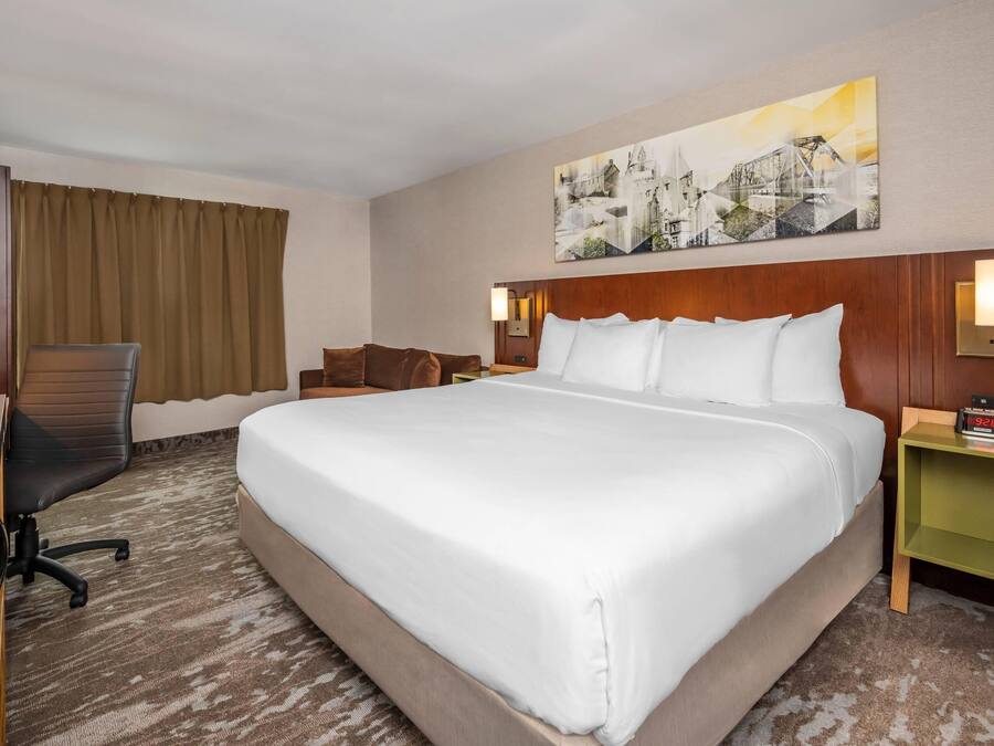 Habitación de hotel con una cama grande, un escritorio con silla, una mesita de noche y un reloj en la pared.