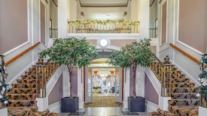 A grand staircase with ornate railings and a chandelier, leading to a second-floor balcony.