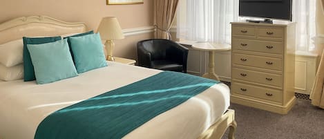 Una habitación de hotel con una cama, televisión, escritorio y silla.