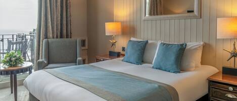 A hotel room with a large bed, two bedside tables, a chair, a small table with a plant, and a view of the ocean.