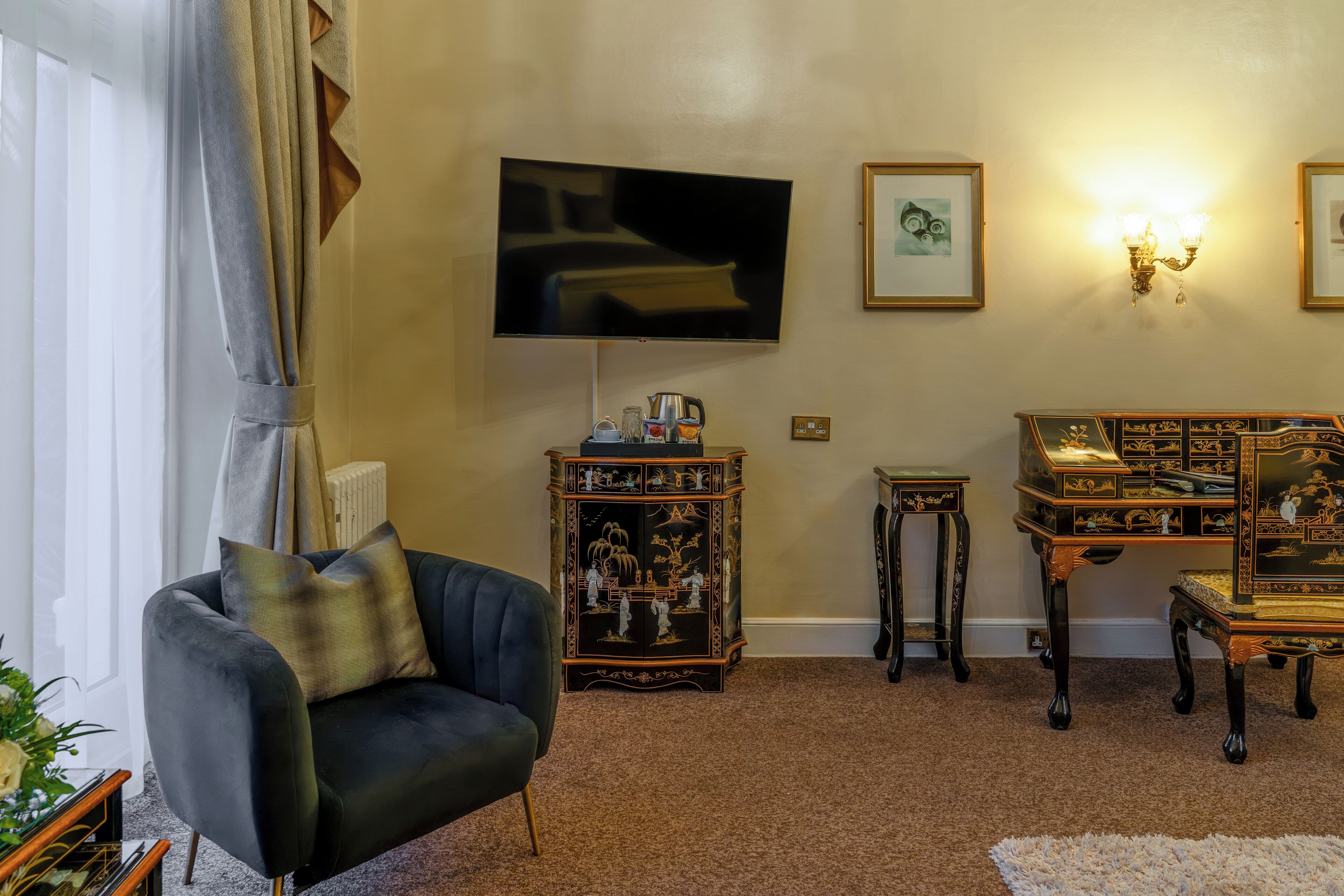 Una sala de estar con un sillón oscuro, un televisor de pantalla plana, un aparador decorativo y una mesita.