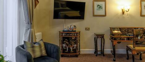 A living room with a dark armchair, a flat-screen TV, a decorative cabinet, and a small table.
