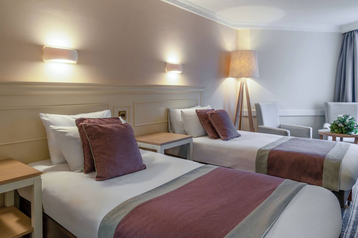Une chambre d’hôtel avec deux lits, chacun doté d’une tête de lit, de tables de chevet et de lampes.