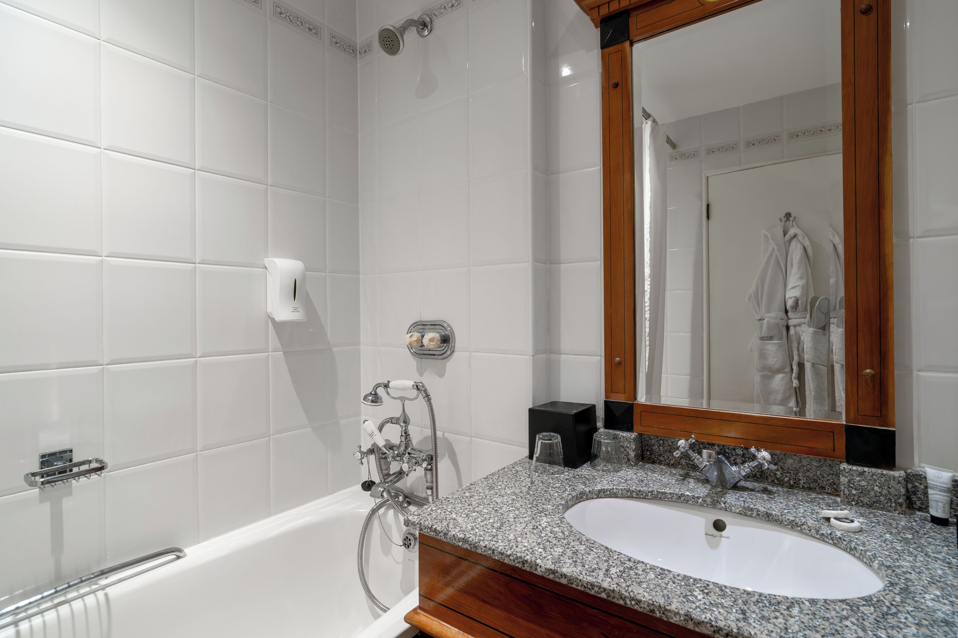 Een moderne badkamer met een wit bad, een wastafel met een granieten aanrechtblad en een grote spiegel.
