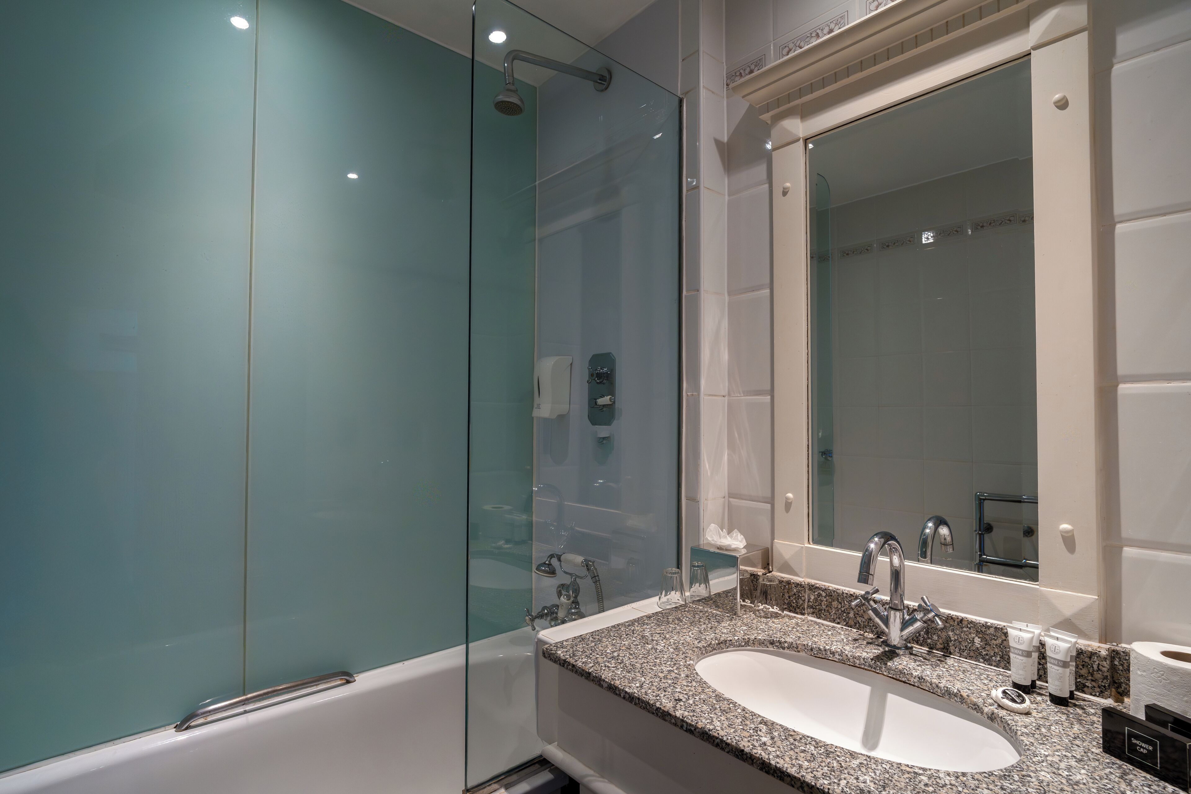 Un baño moderno con cabina de ducha de vidrio, lavabo con encimera de granito y un espejo grande.
