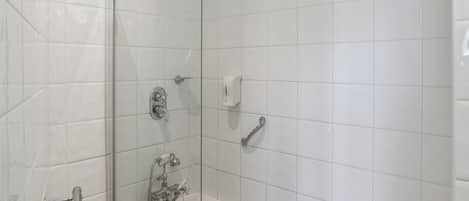 A modern bathroom with white tiles, a glass shower enclosure, a bathtub, and a hand dryer.
