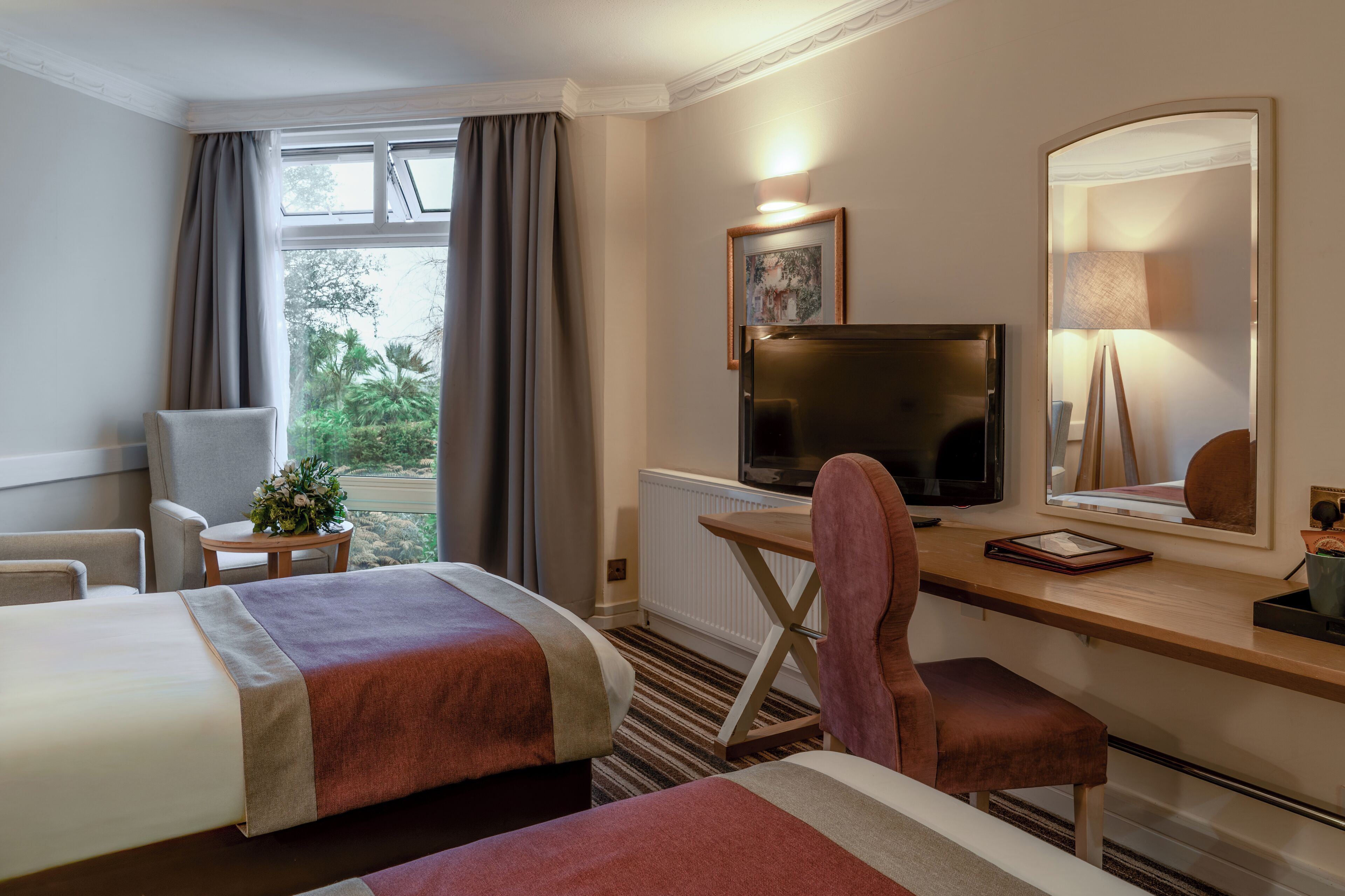 Habitación de hotel con dos camas, un escritorio con computadora, televisor y un espejo grande.
