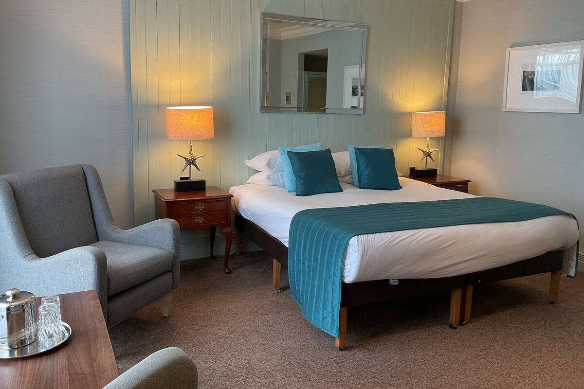 Une chambre d’hôtel avec un lit, deux tables de chevet, une chaise et une petite table.