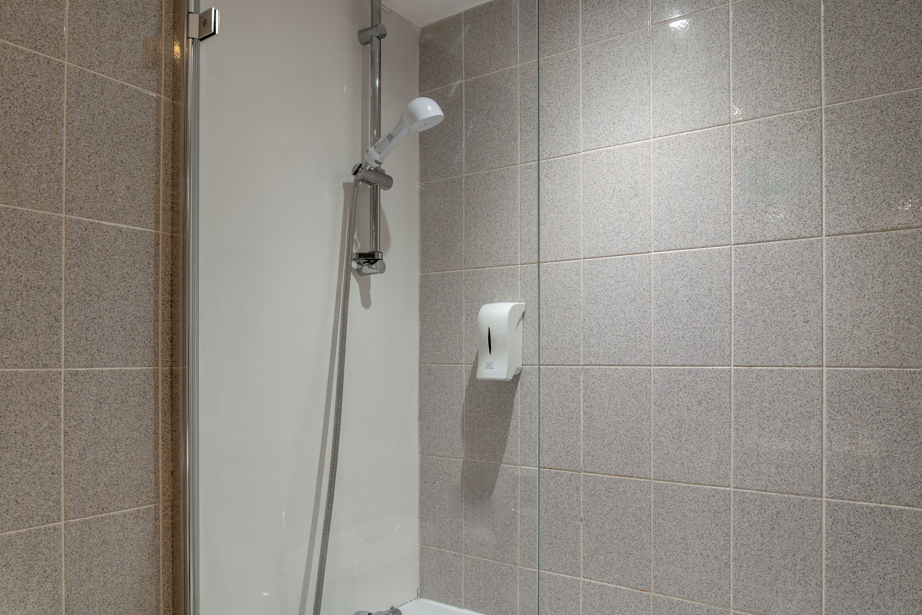 Una ducha con cabezal de ducha de mano y llave instalada en la pared.