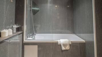 A modern bathroom with a glass-enclosed shower, a white bathtub, and a marble wall.