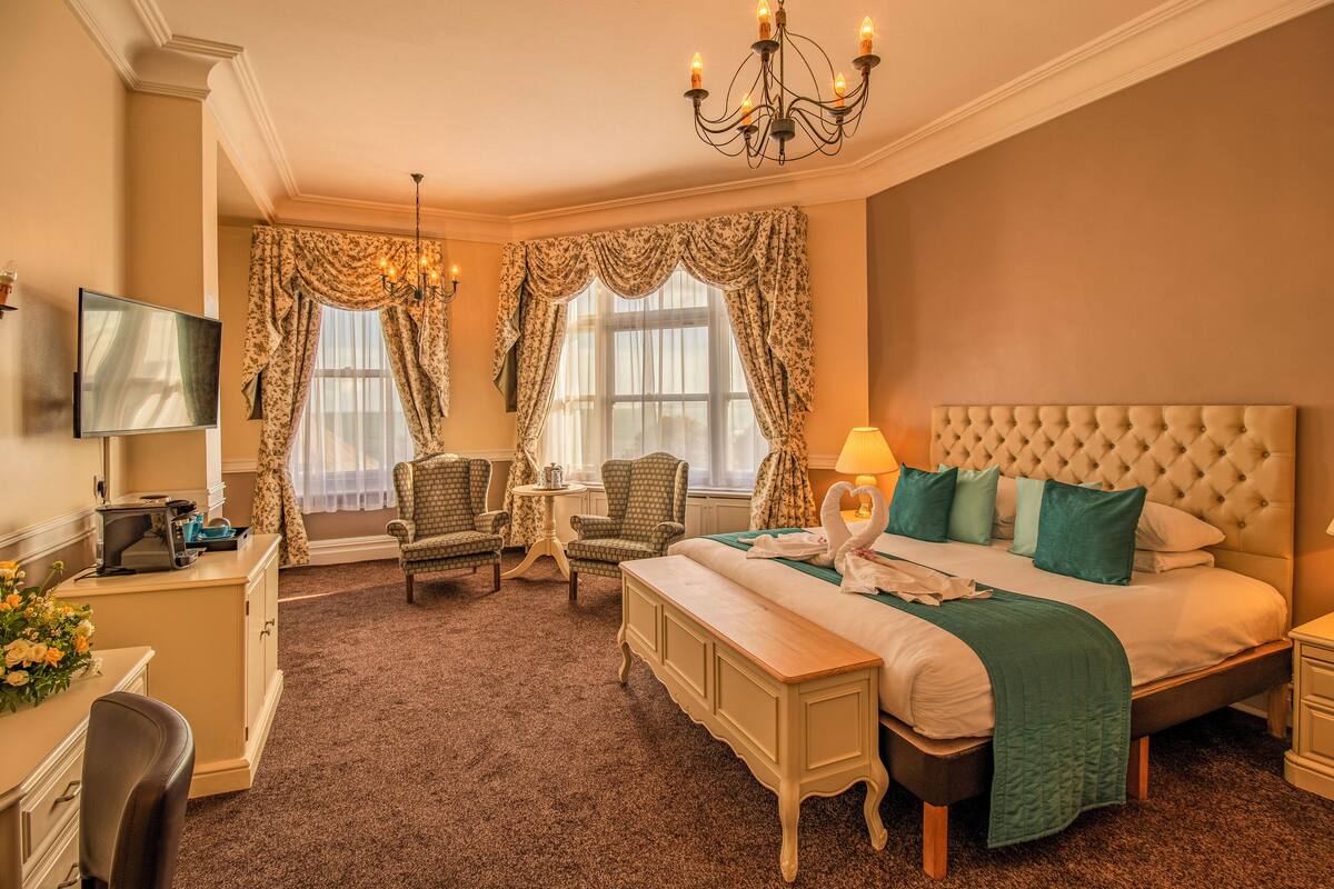 Une chambre d’hôtel avec un grand lit, un bureau avec un ordinateur, une chaise, une télévision et un lustre.