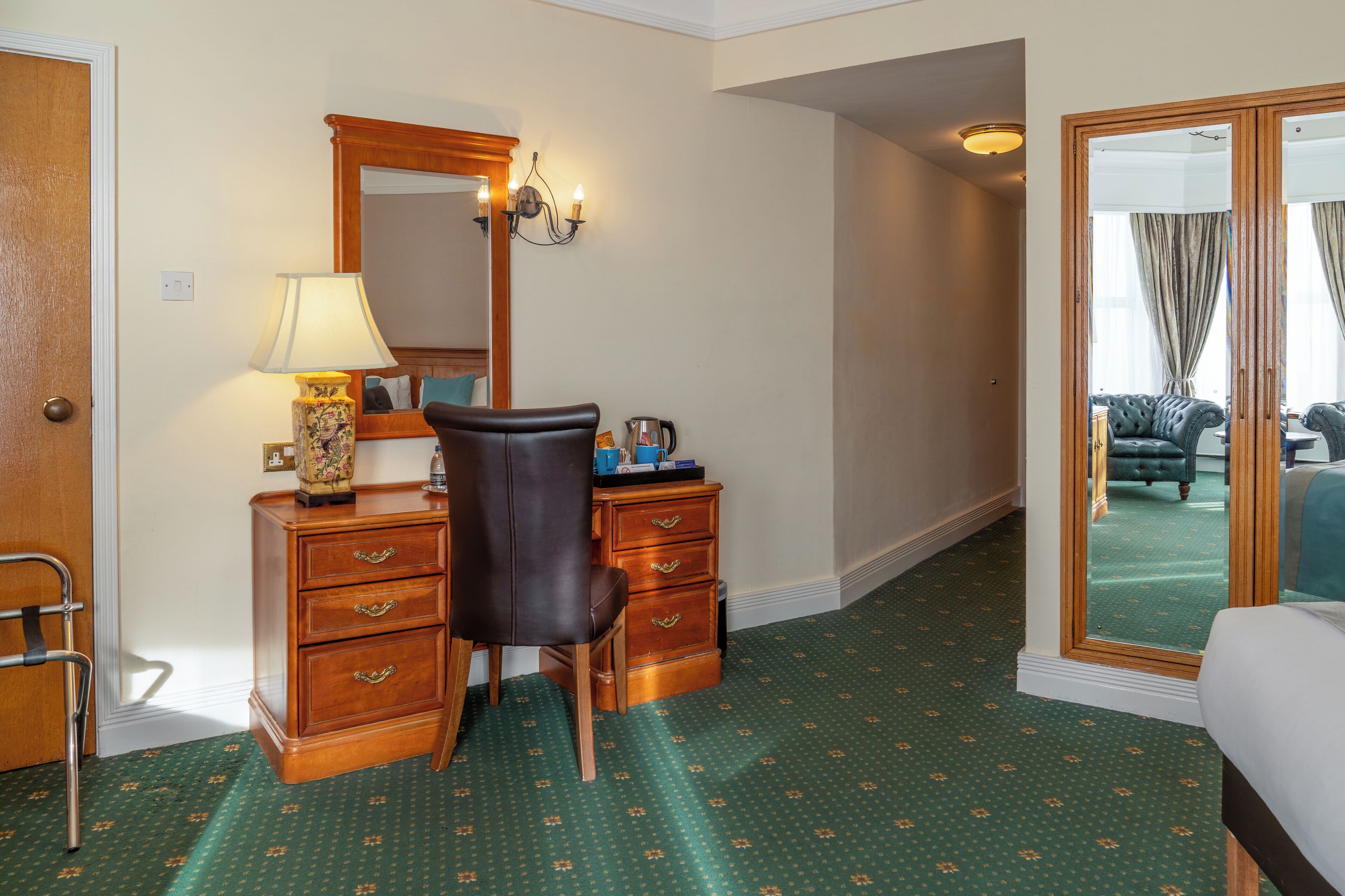 Ein Hotelzimmer mit einem Holztisch, einem Sessel, einem Schminktisch und einem großen Spiegel an der Wand.