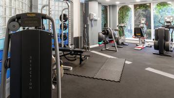 Un gimnasio con equipo de levantamiento de pesas, máquinas de cardio y vistas a zonas verdes a través de amplias ventanas.