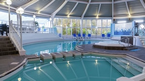 An indoor swimming pool with a covered area, stairs, lounge chairs, and a hot tub.