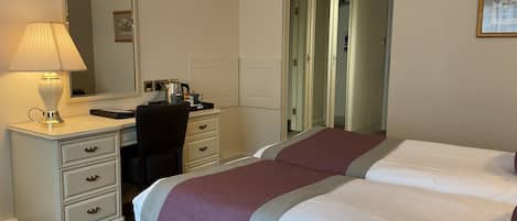 Una habitación de hotel con dos camas, un escritorio con lámpara, una silla, un aparador y un espejo.