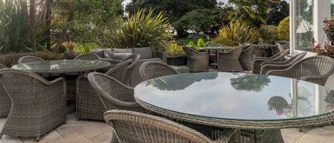 An outdoor patio with wicker furniture, a glass table, and potted plants.