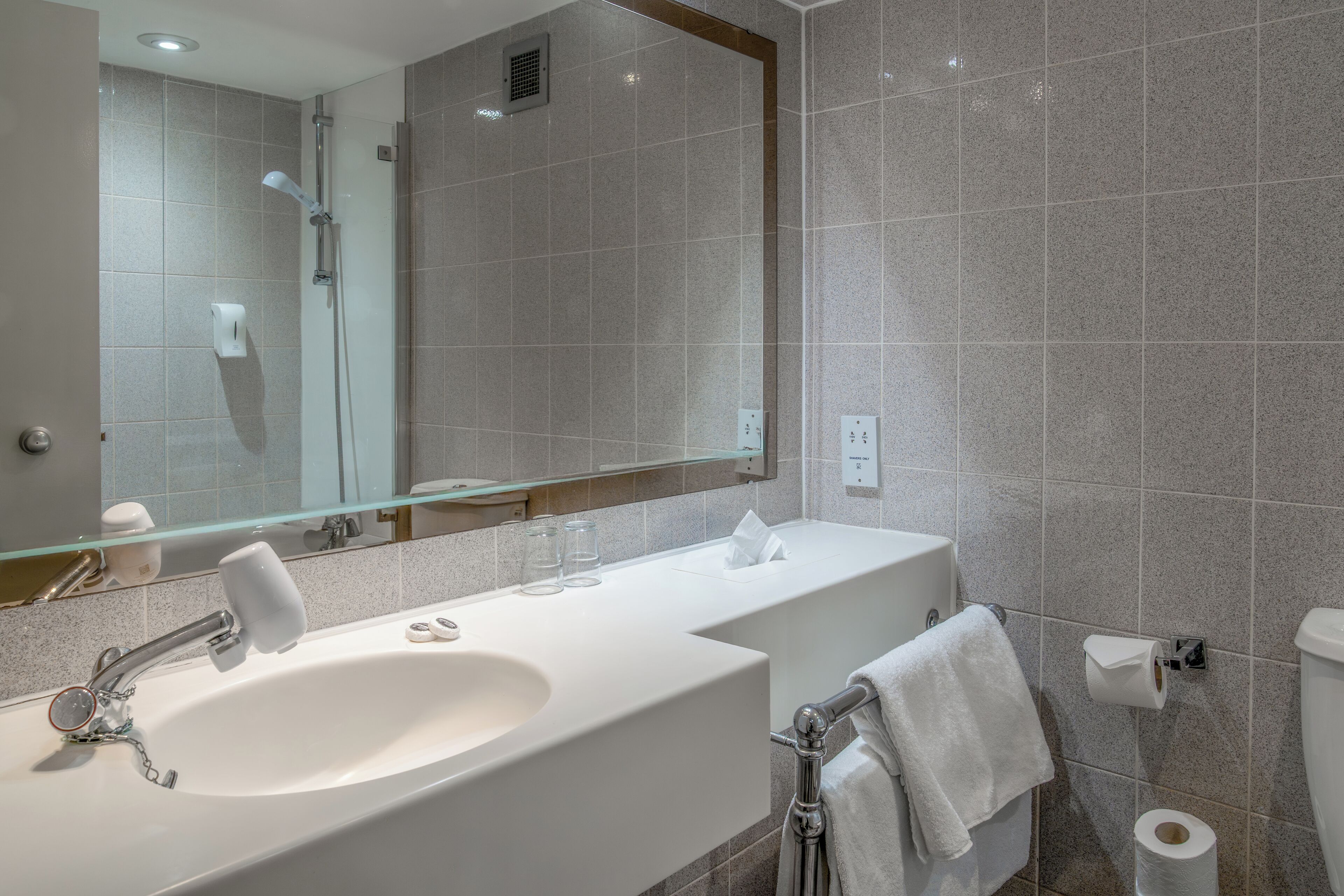 A modern bathroom with a large mirror, two sinks, a shower, and a toilet.