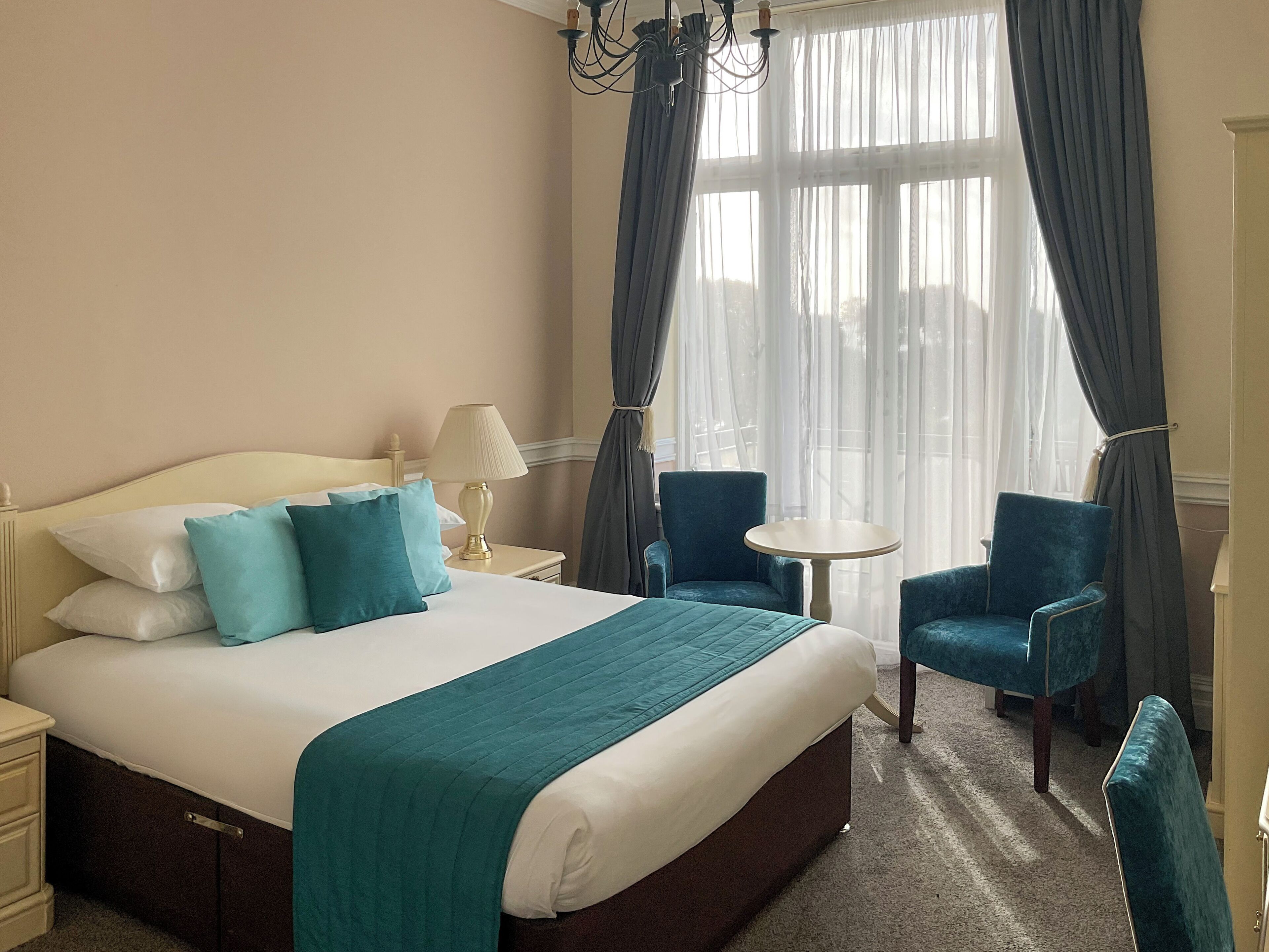 Una habitación de hotel con una cama, dos sillas, una mesita y una lámpara.