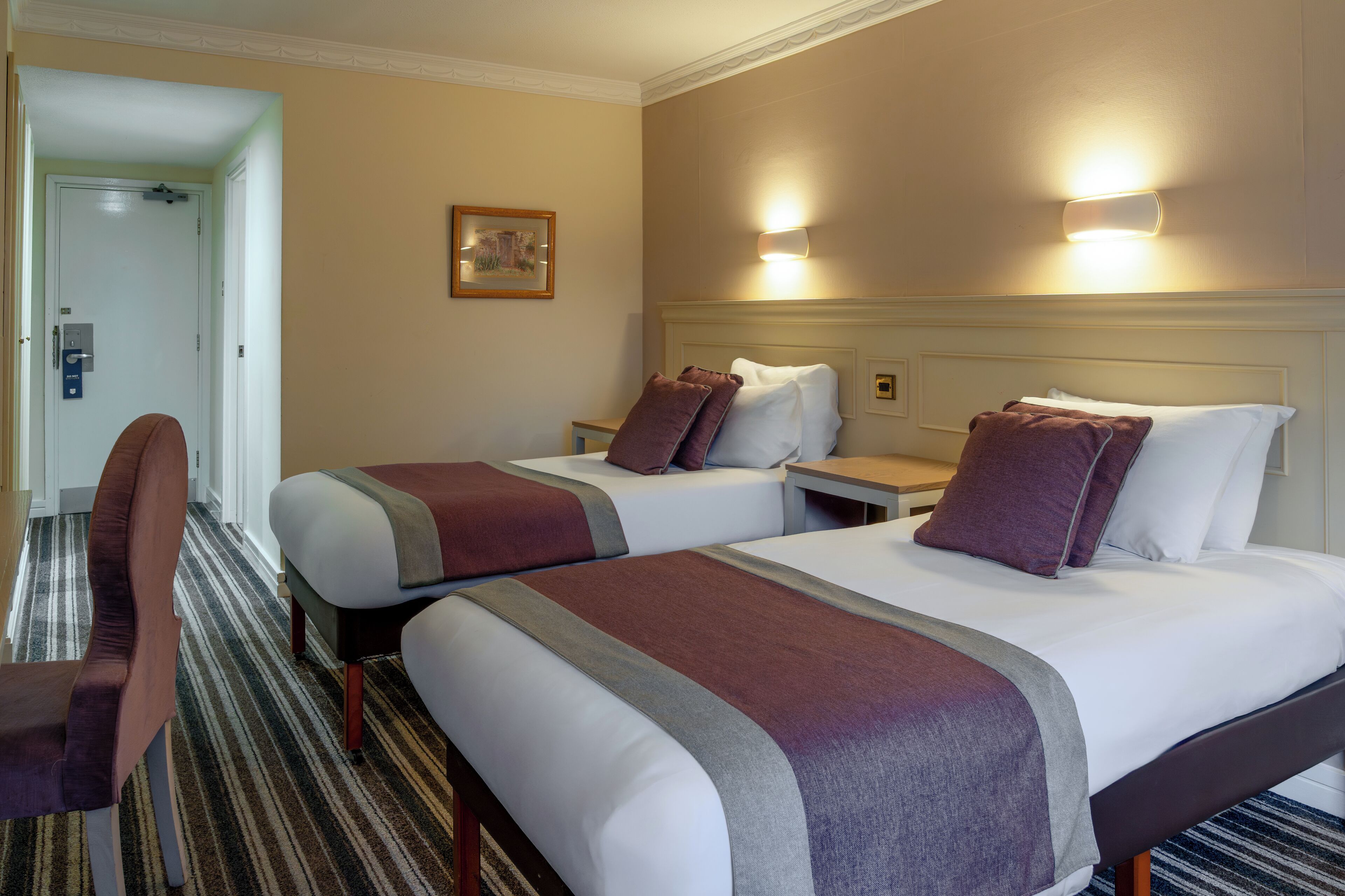 A hotel room with two beds, a chair, and a small table.