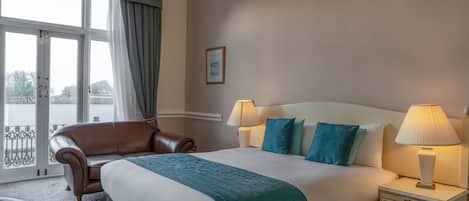 A hotel room with a large bed, two bedside lamps, a brown leather chair, and a view through a large window.