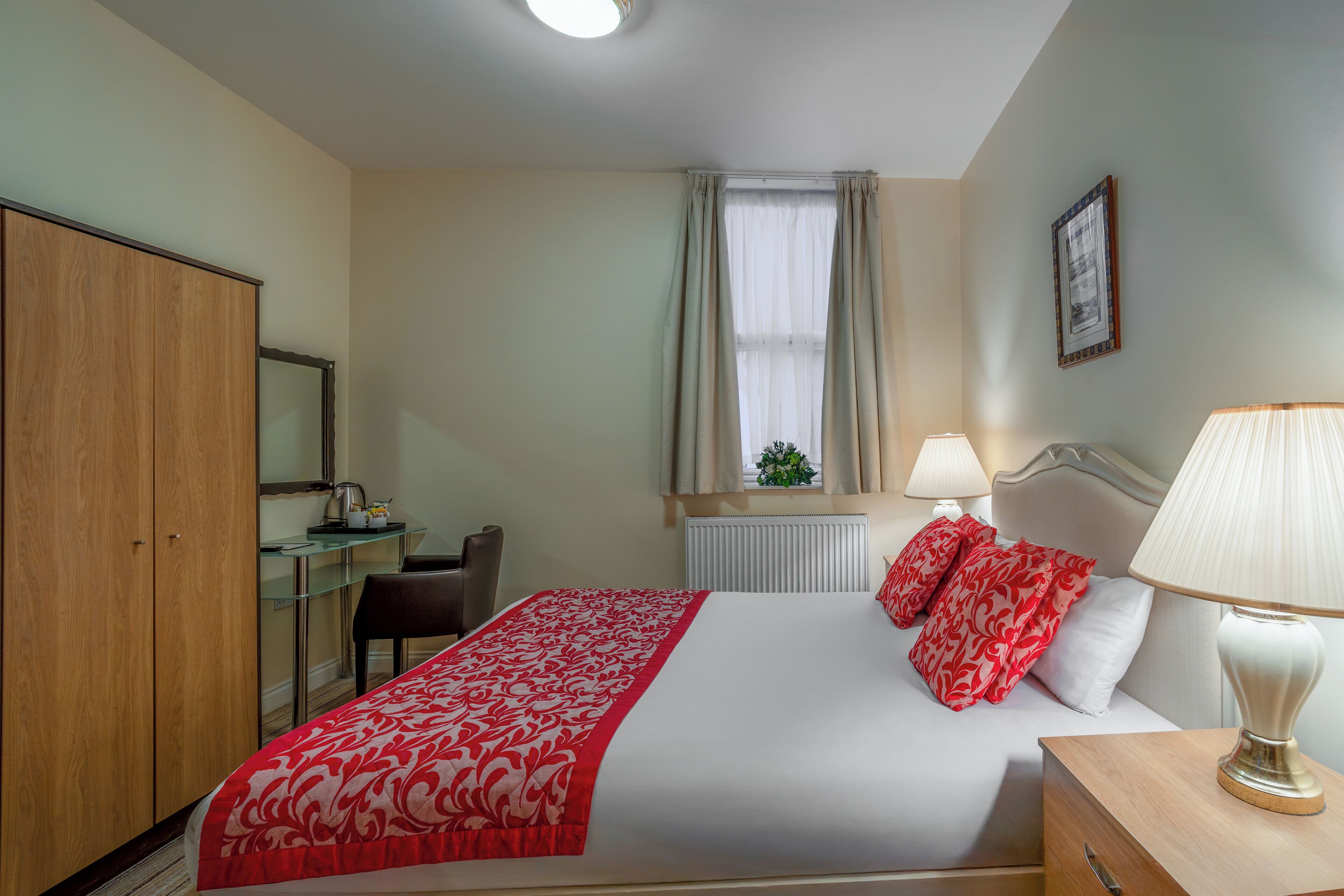 Ein Hotelzimmer mit Bett, Schreibtisch, Stuhl, Kleiderschrank, einem Fenster mit Vorhängen und einer Lampe.