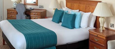 A neatly arranged hotel room with a large bed, two bedside tables, a chair, a desk, and a chandelier.