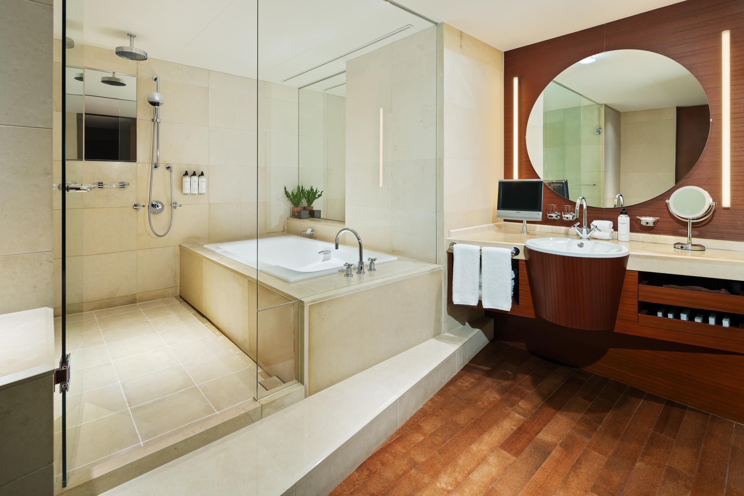 Ein modernes Badezimmer mit einer gläsernen Duschkabine, einer großzügigen Badewanne und einem hölzernen Waschtisch mit rundem Spiegel.