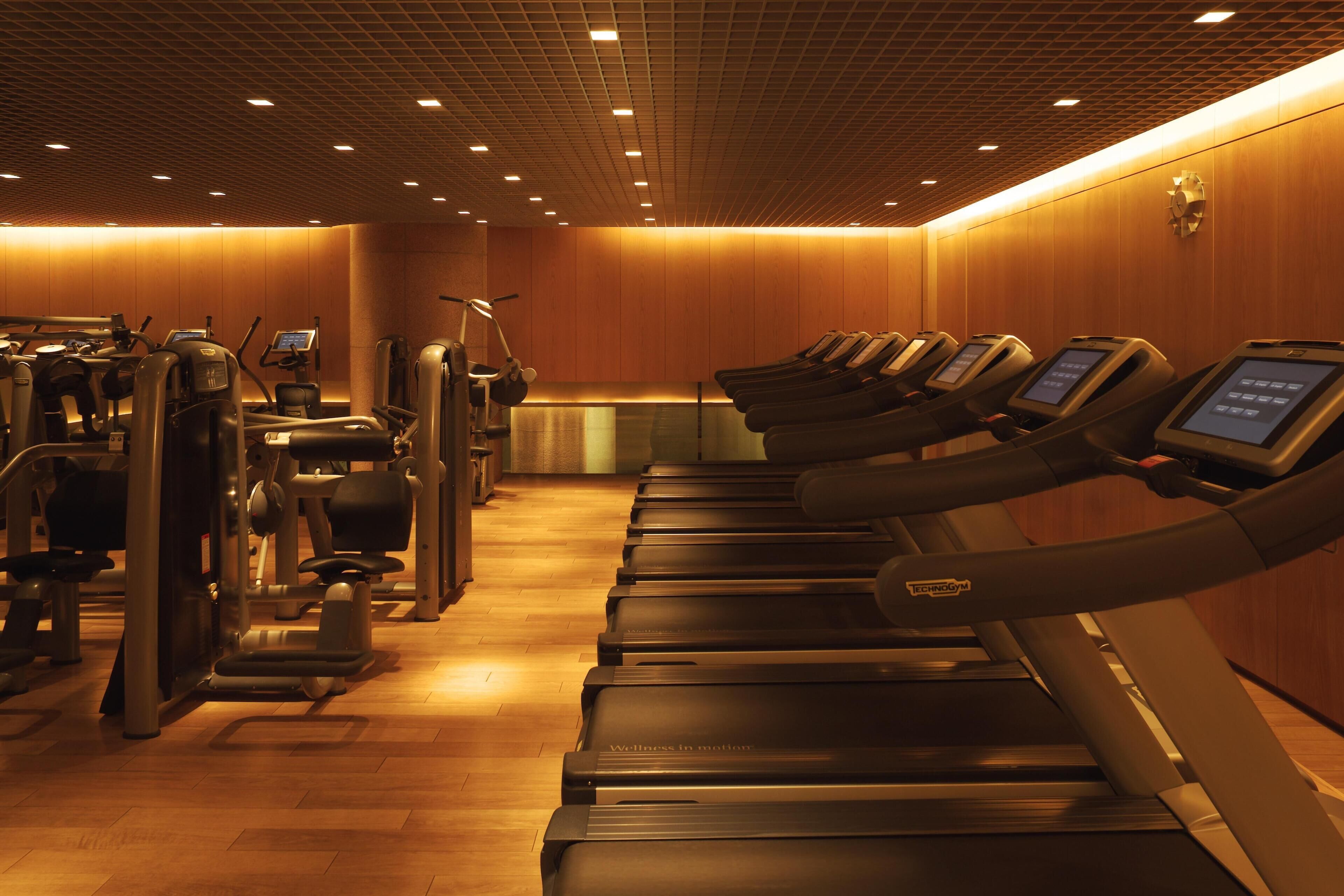 A gym with treadmills, exercise machines, and a wooden wall.