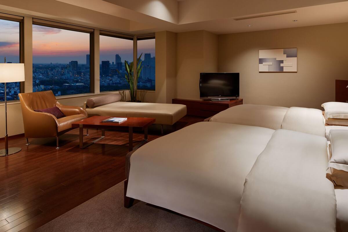 A hotel room with a large bed, a sofa, a TV, and a city view.
