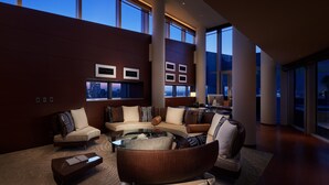 A spacious living room with a modern design, featuring a large sofa set, a coffee table, and a city view through large windows.