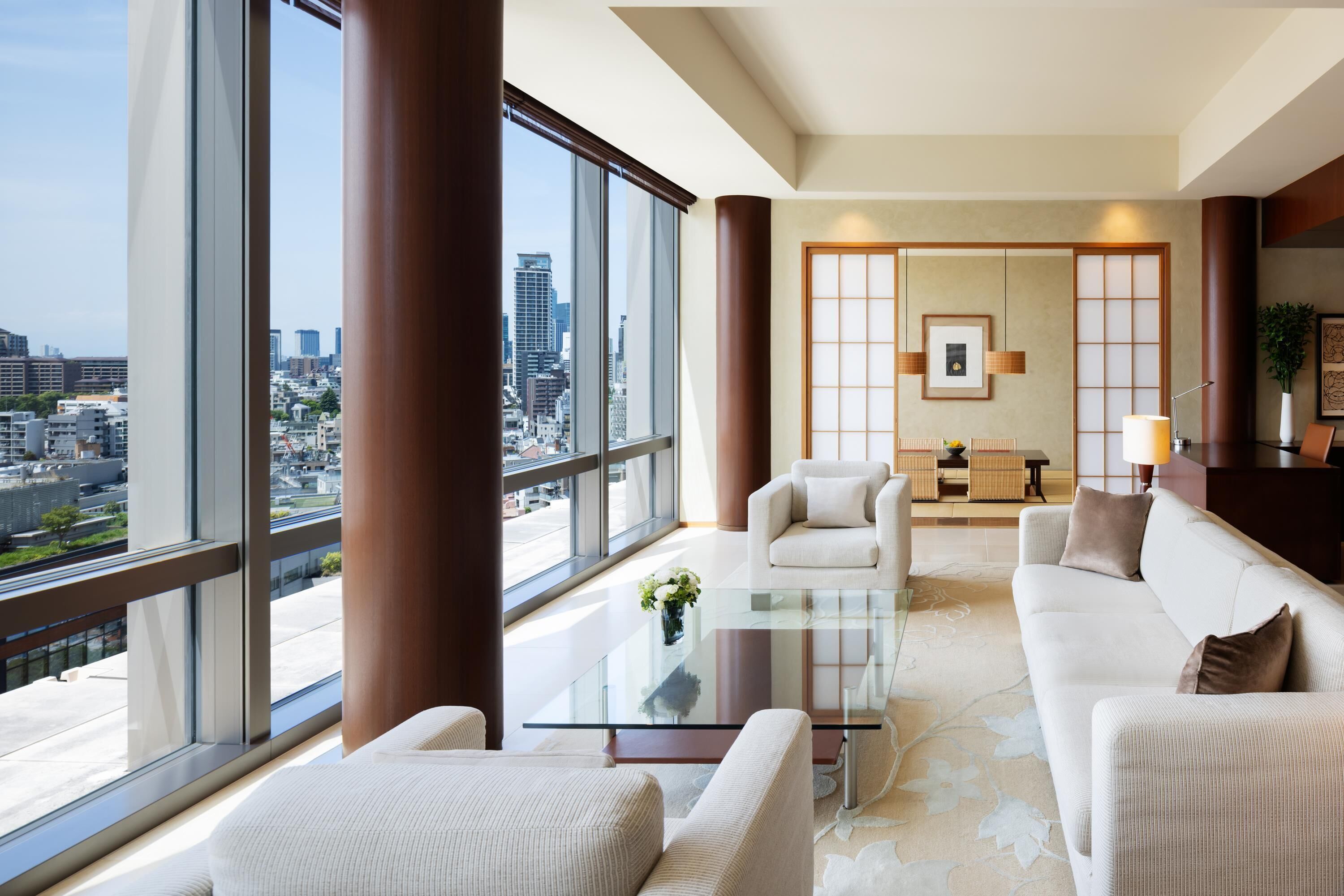 A modern living room with a glass coffee table, a sofa, and a view of the city through large windows.