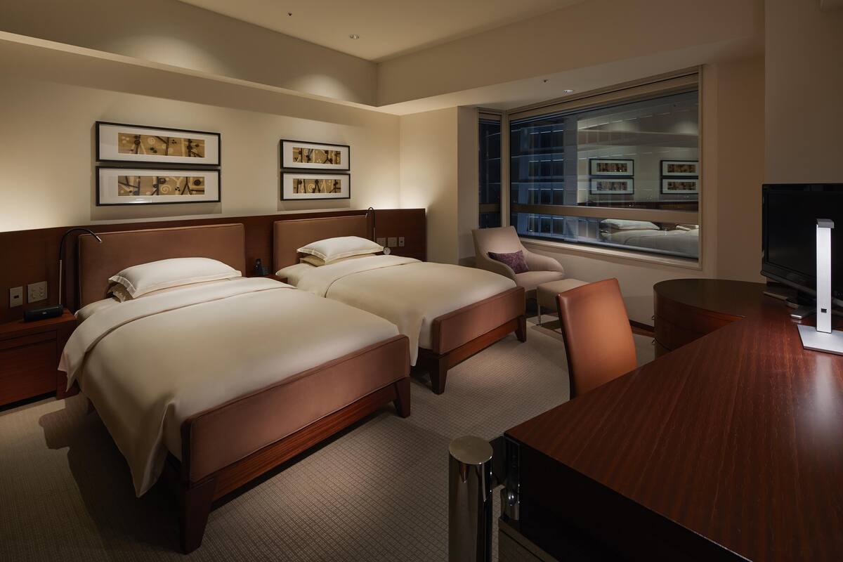 A hotel room with two beds, a desk, a chair, a TV, and framed pictures on the wall.