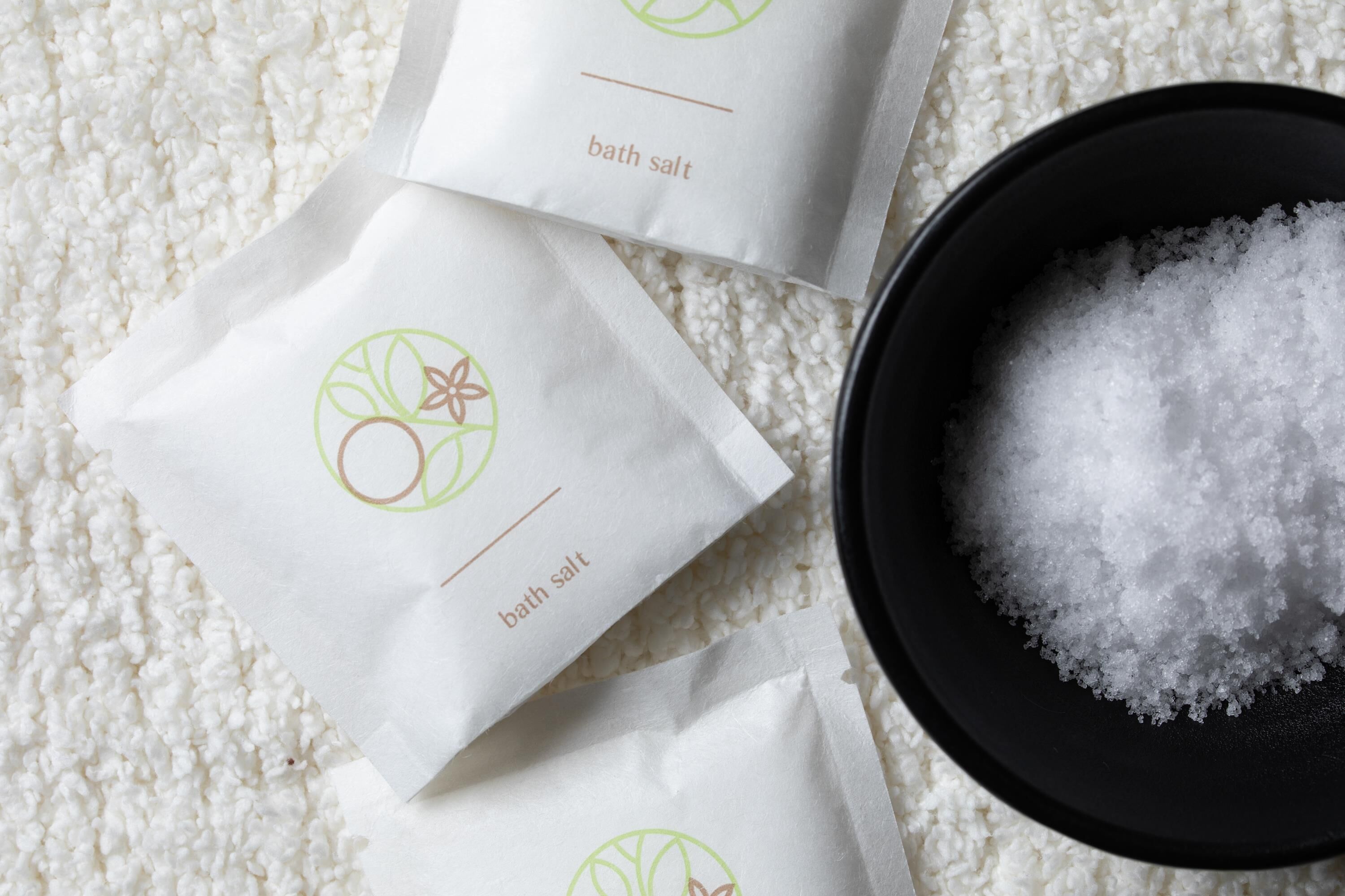 Three white paper bags labeled 'bath salt' and a black bowl filled with white bath salts.