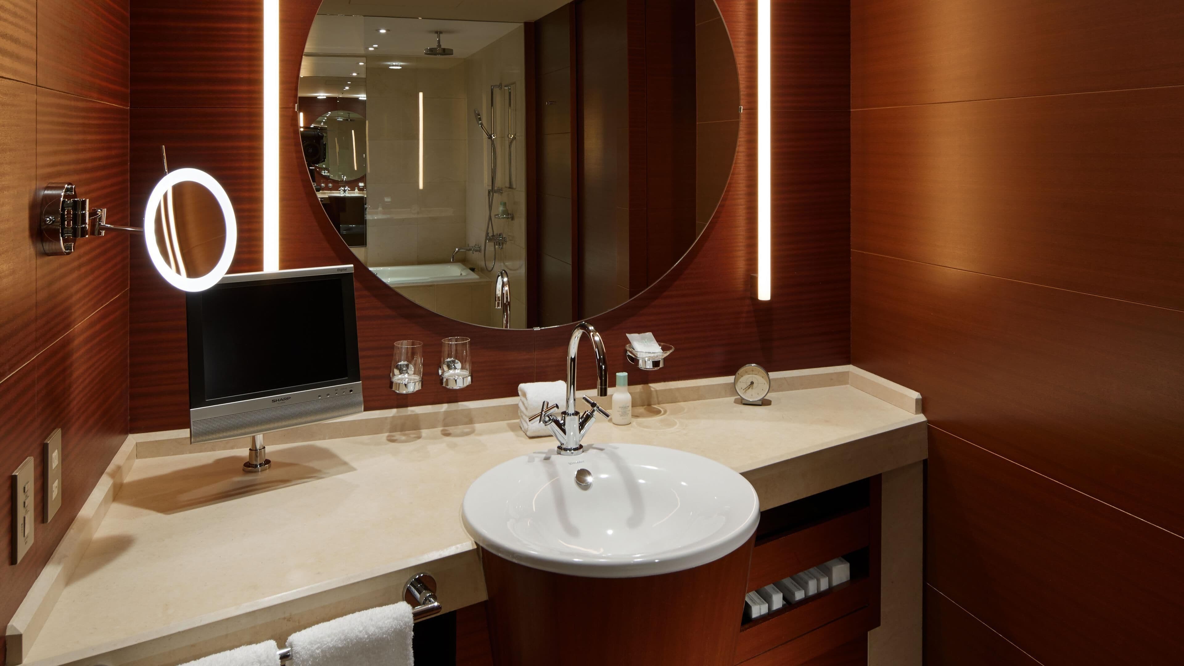 A modern bathroom with a round mirror, a sink, a handheld showerhead, and a handheld radio.