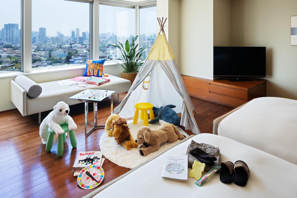 A cozy room with a city view, a sofa, a small table with toys, a teepee, and a TV.