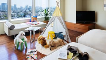 A cozy room with a city view, a sofa, a small table with toys, a teepee, and a TV.