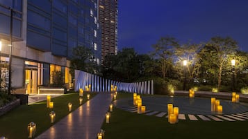 A modern building with a glass facade, a well-lit pathway, and a landscaped area with trees and illuminated bollards.