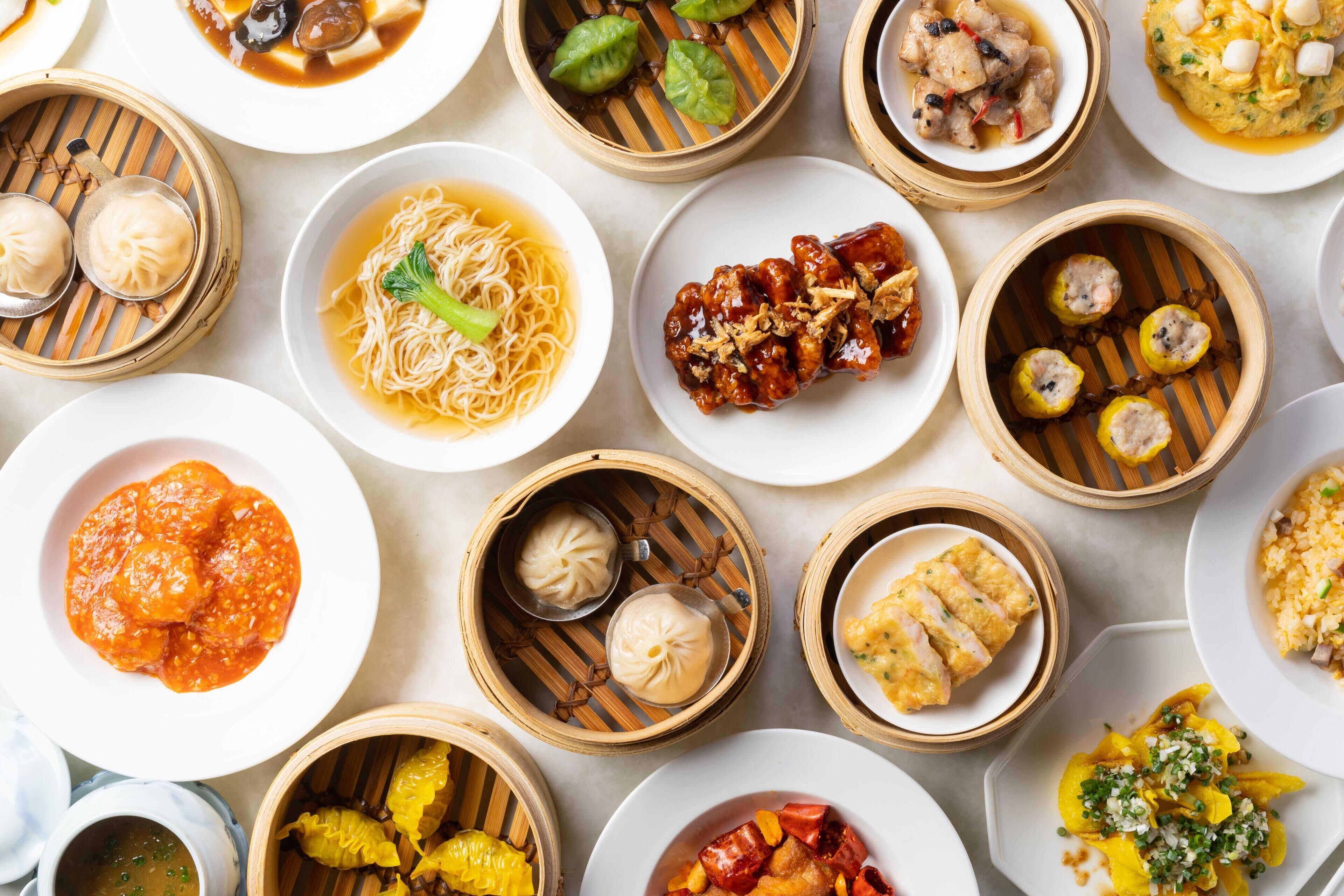 Une variété de plats asiatiques, notamment des raviolis et des nouilles, servis dans des assiettes et dans des paniers à vapeur en bambou.