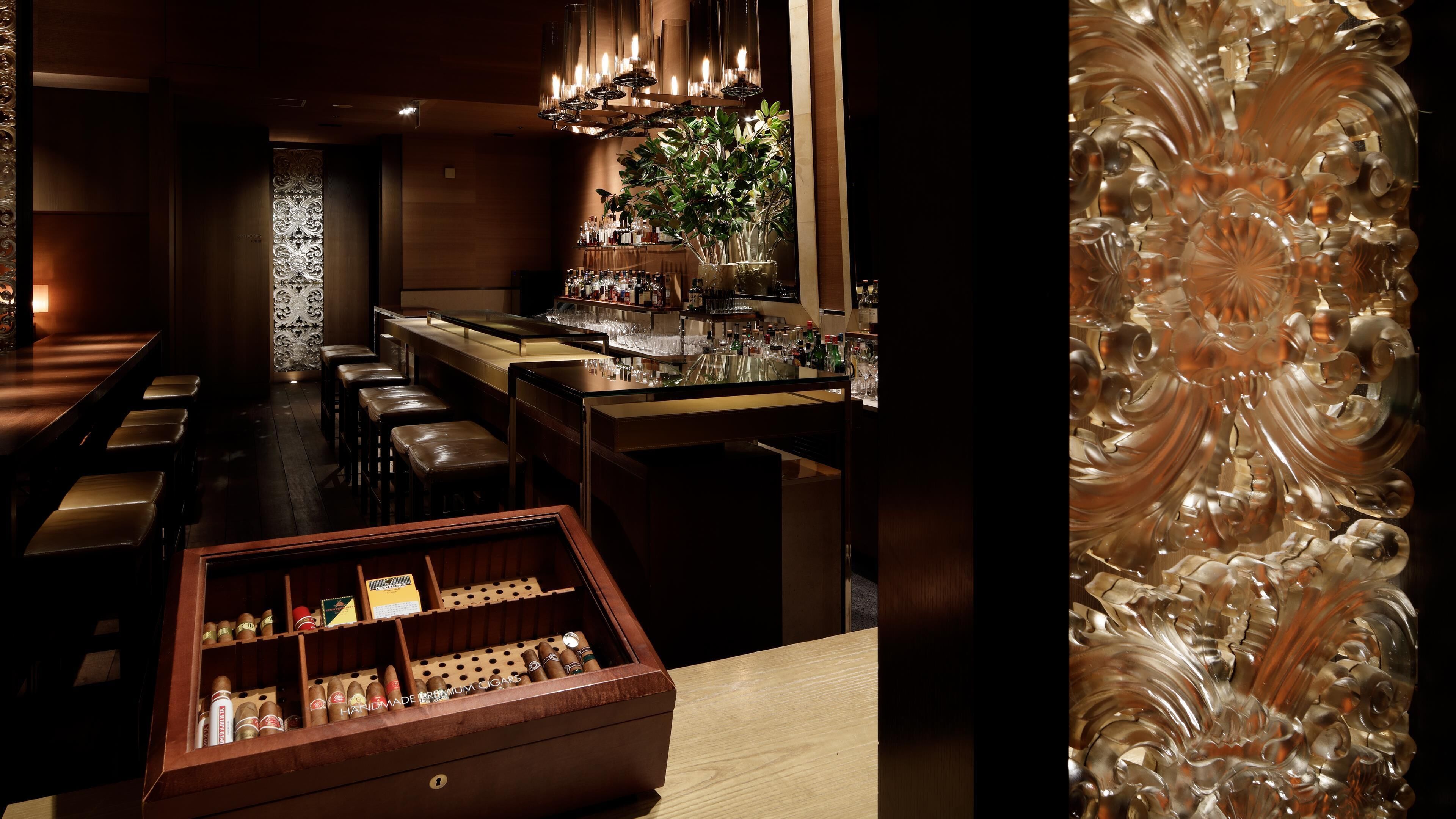 A bar area with stools, a bar counter, and a display of cigars.