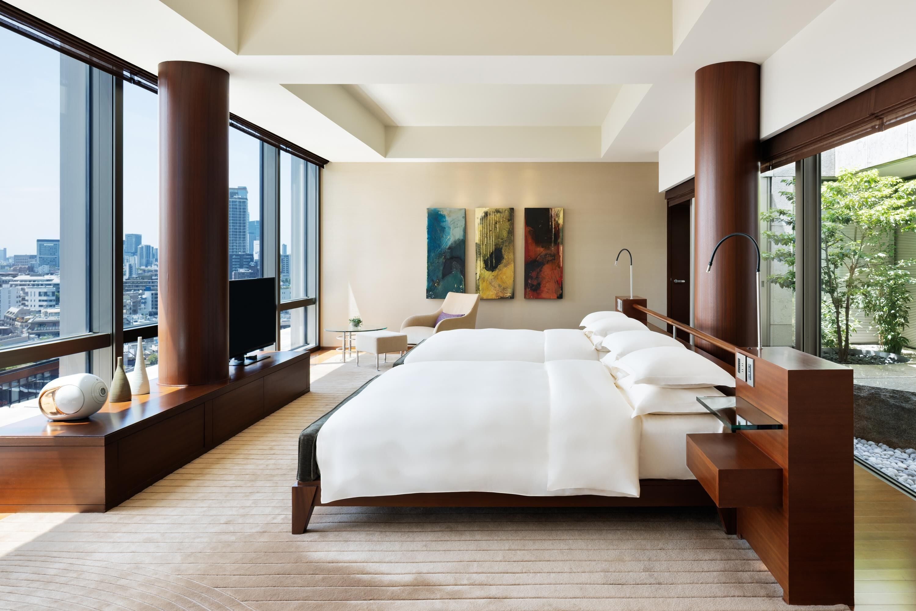 A modern bedroom with a large bed, city views, and artwork on the wall.