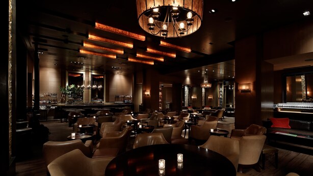 A dimly lit bar area with leather chairs, a bar counter, and a chandelier. - Grand Hyatt Tokyo (Tokyo)