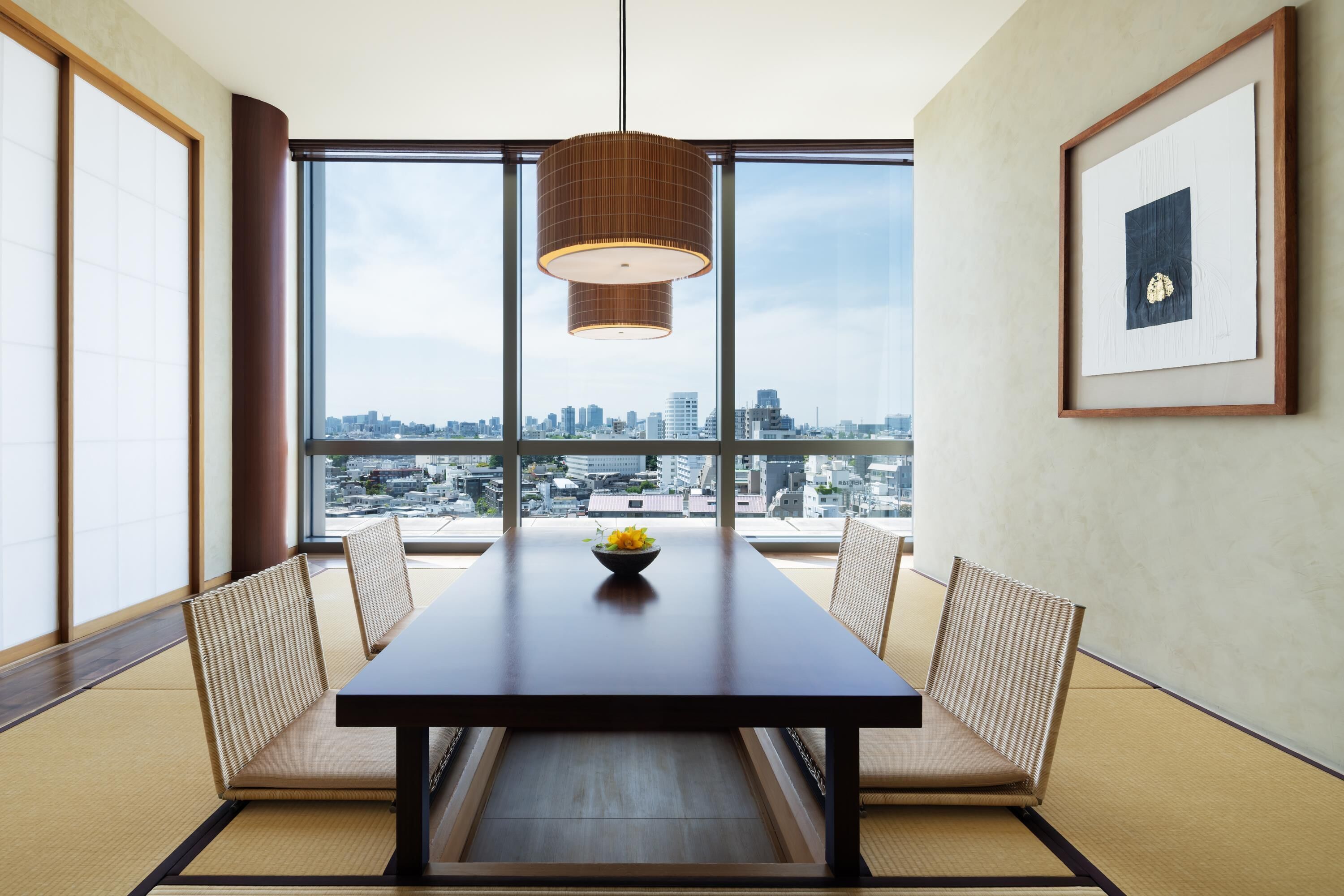 A dining area with a table, chairs, a hanging light fixture, and a framed picture on the wall.