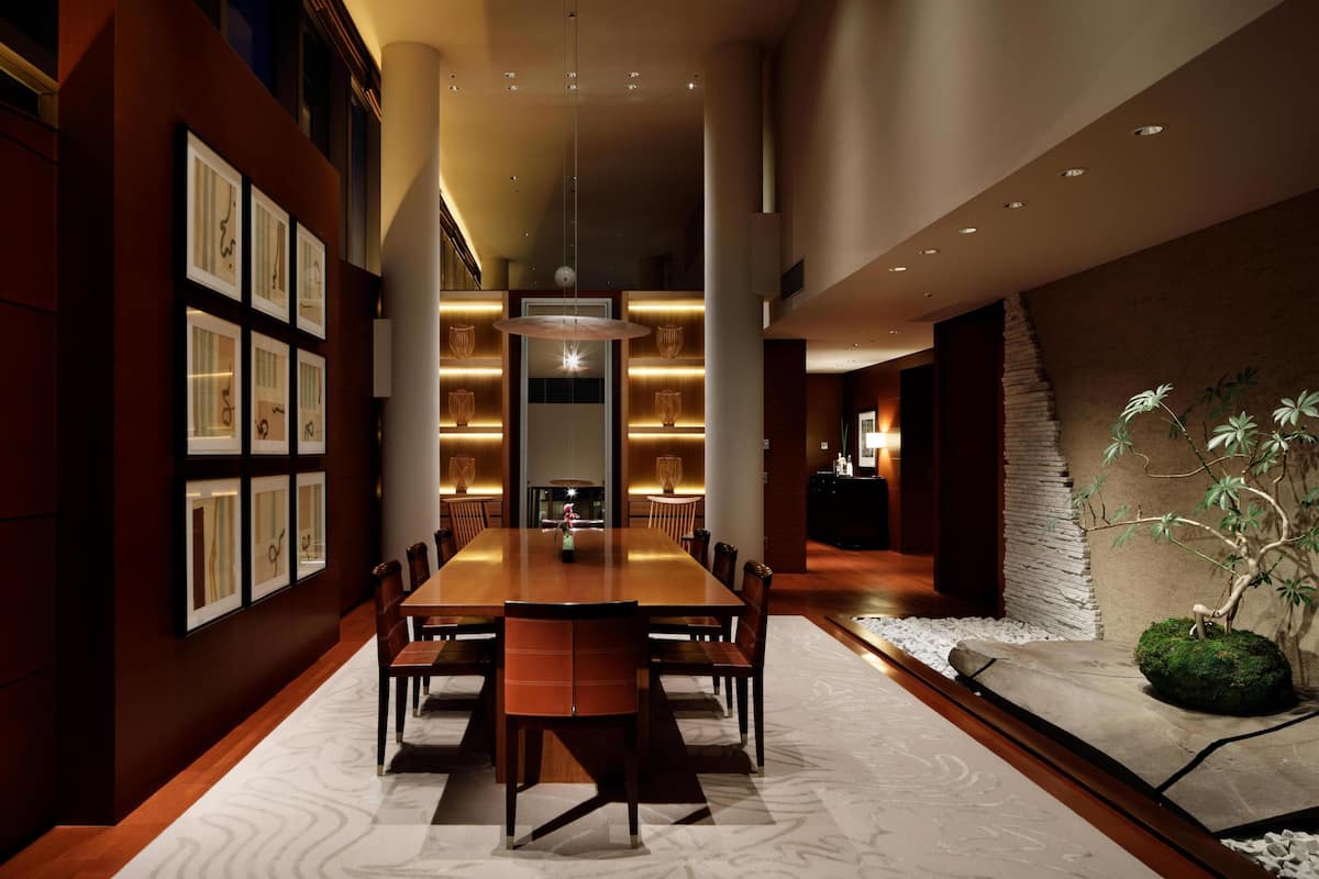 A modern dining area with a long table, chairs, and a central light fixture.