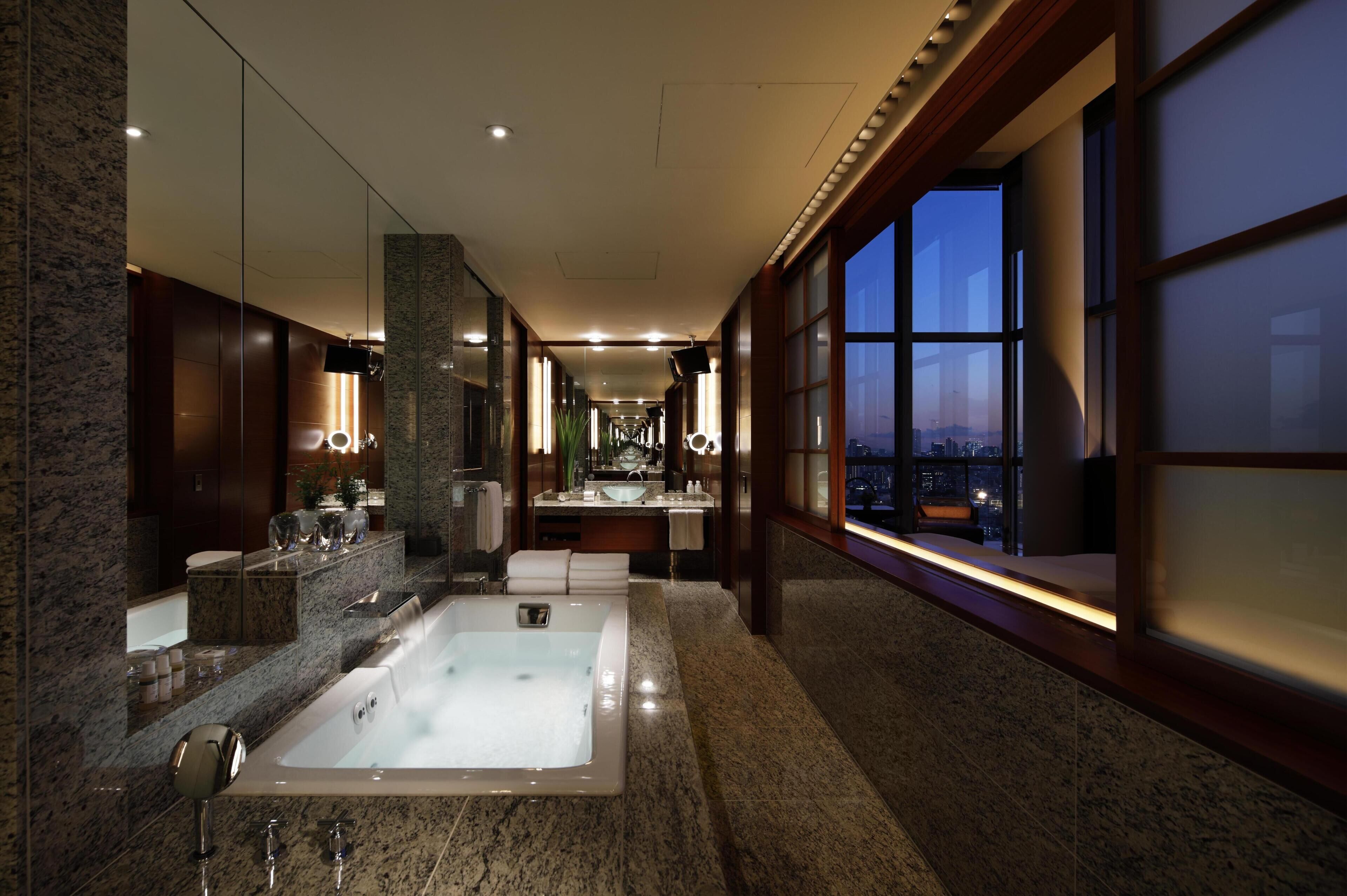 A modern bathroom with a large bathtub, a vanity with a mirror, and a window with a city view.