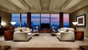 A modern living room with a large TV, two sofas, a coffee table, and a city view through large windows.