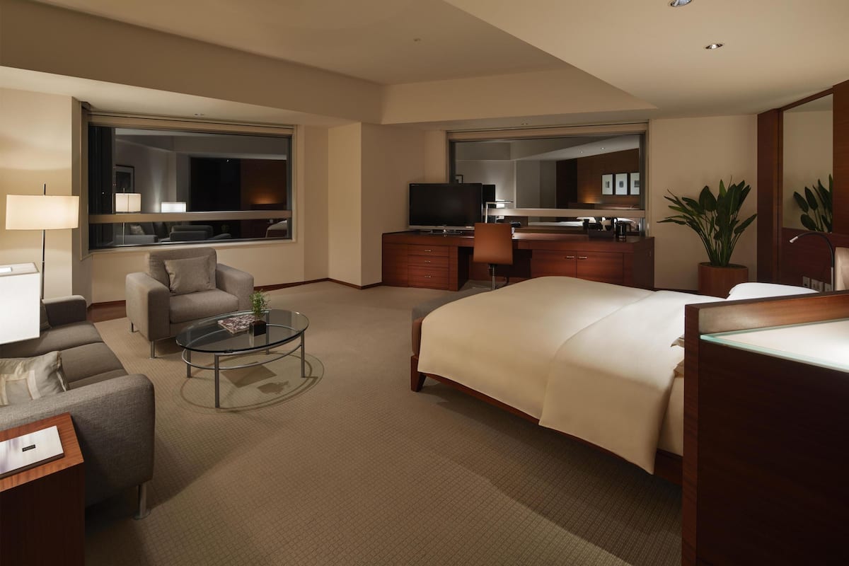 A hotel room with a bed, a desk, a television, a sofa, a coffee table, and a large window.
