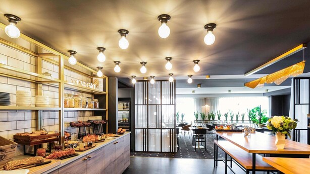 Una cocina moderna con armarios de madera, una isla central con alimentos y un comedor con mesas y sillas.