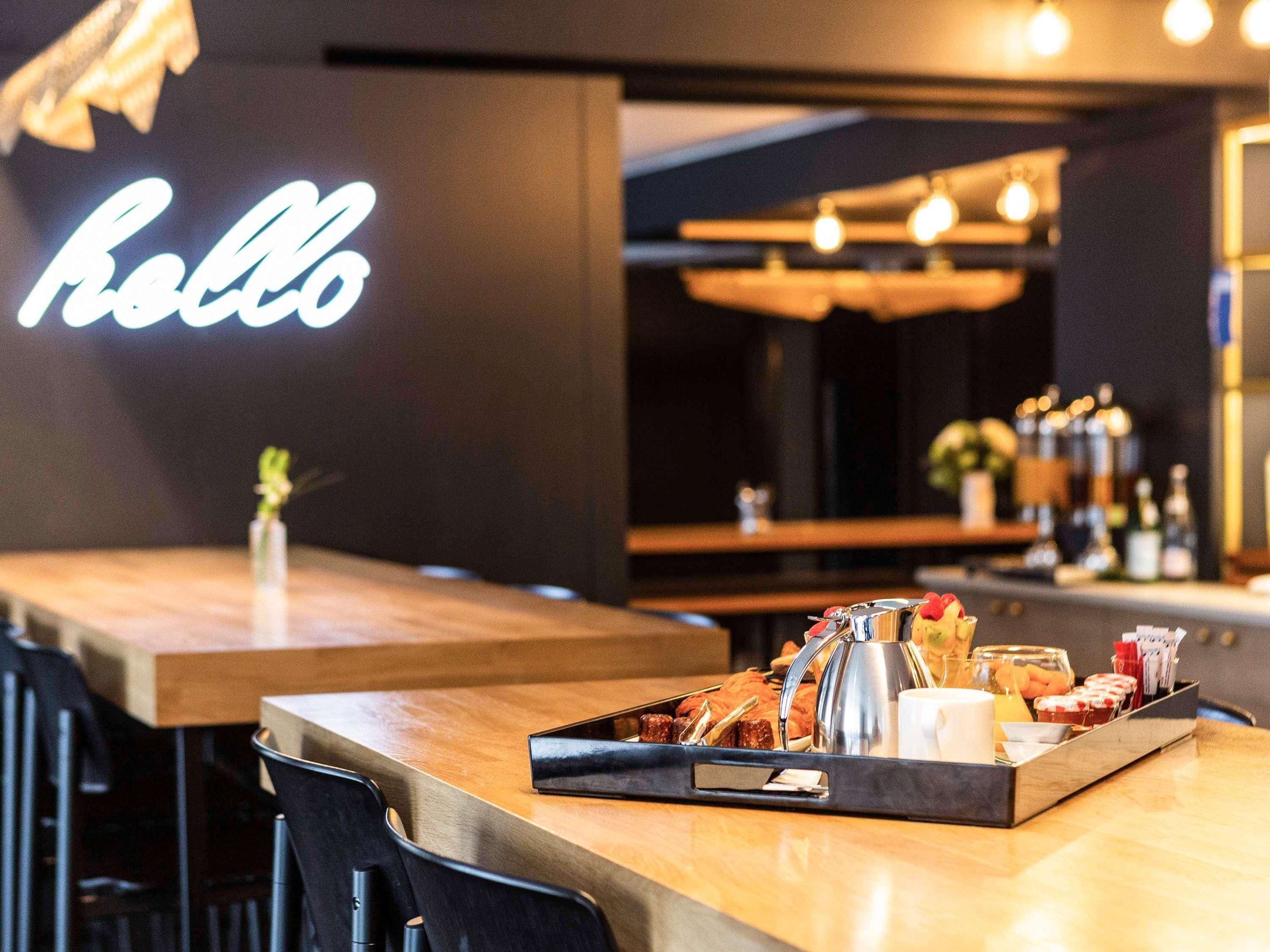 Un coin bar avec un panneau néon indiquant le mot « Rolls », un plateau rempli de collations et une cafetière.